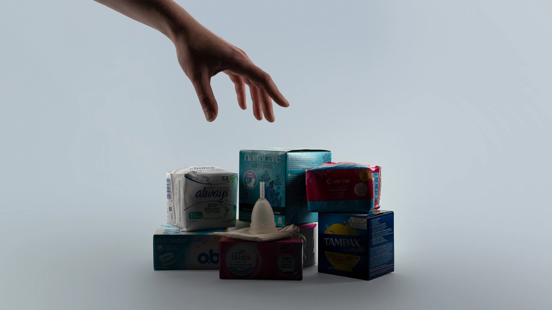 Hand reaching for a selection of period products, including pads, tampons and menstrual cup